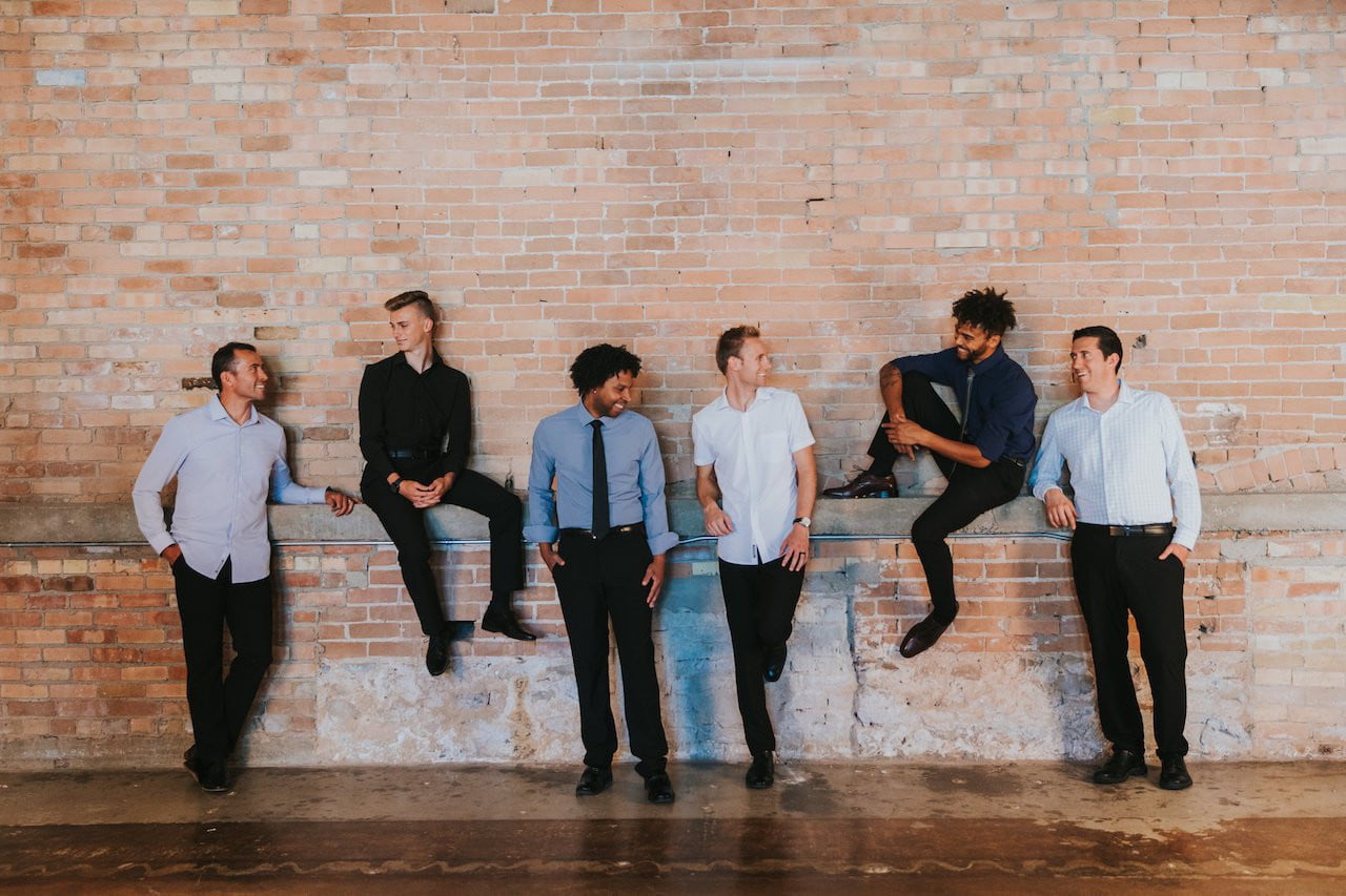 Six men wearing professional truwear business clothes for men leaning up against a brick wall